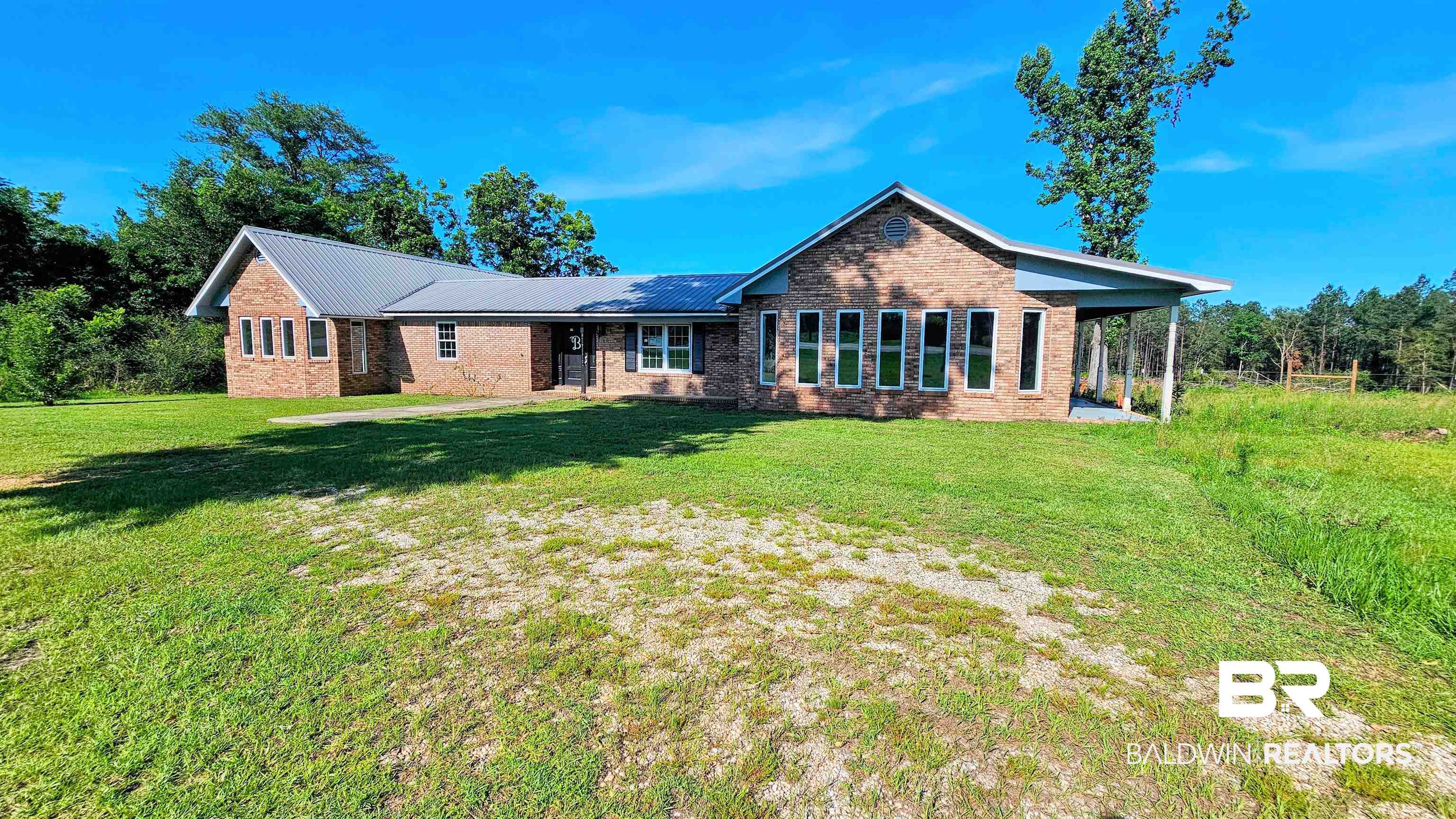 18824 Highway 41 Brewton, AL 36426 - Photo 1 of 40 Brick exterior with a metal roof, featuring multiple windows, a covered entryway, and a covered side patio