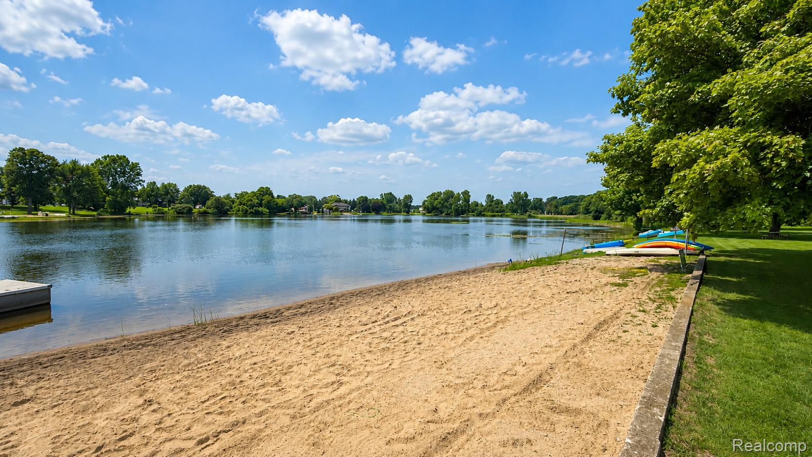 26945 Milford Road, Unit 34 New Hudson, MI 48165 - Photo 6 of 16 Private sand beach with lake frontage, a floating dock, and mature trees bordering a grassy area
