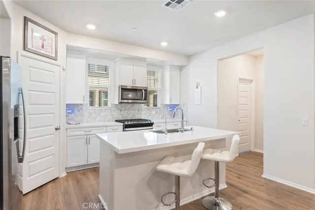 a kitchen with stainless steel appliances a stove a sink refrigerator and white cabinets with wooden floor