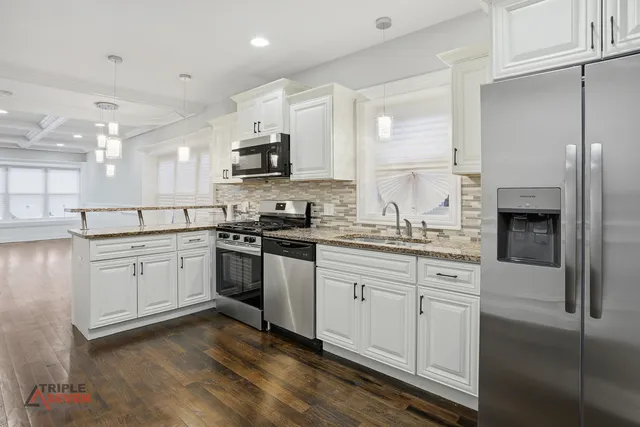 a kitchen with stainless steel appliances granite countertop a sink a stove a refrigerator and white cabinets