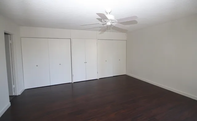 an empty room with wooden floor closet and fan