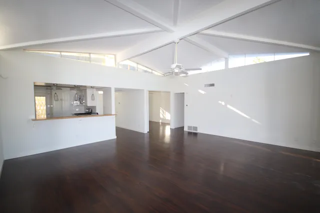 a view of an empty room with wooden floor and kitchen view