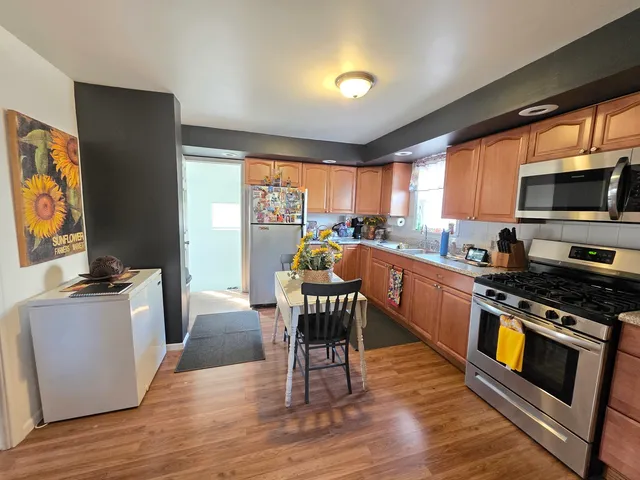 a kitchen with stainless steel appliances a stove a sink dishwasher a microwave oven with a dining table and chairs with wooden floor