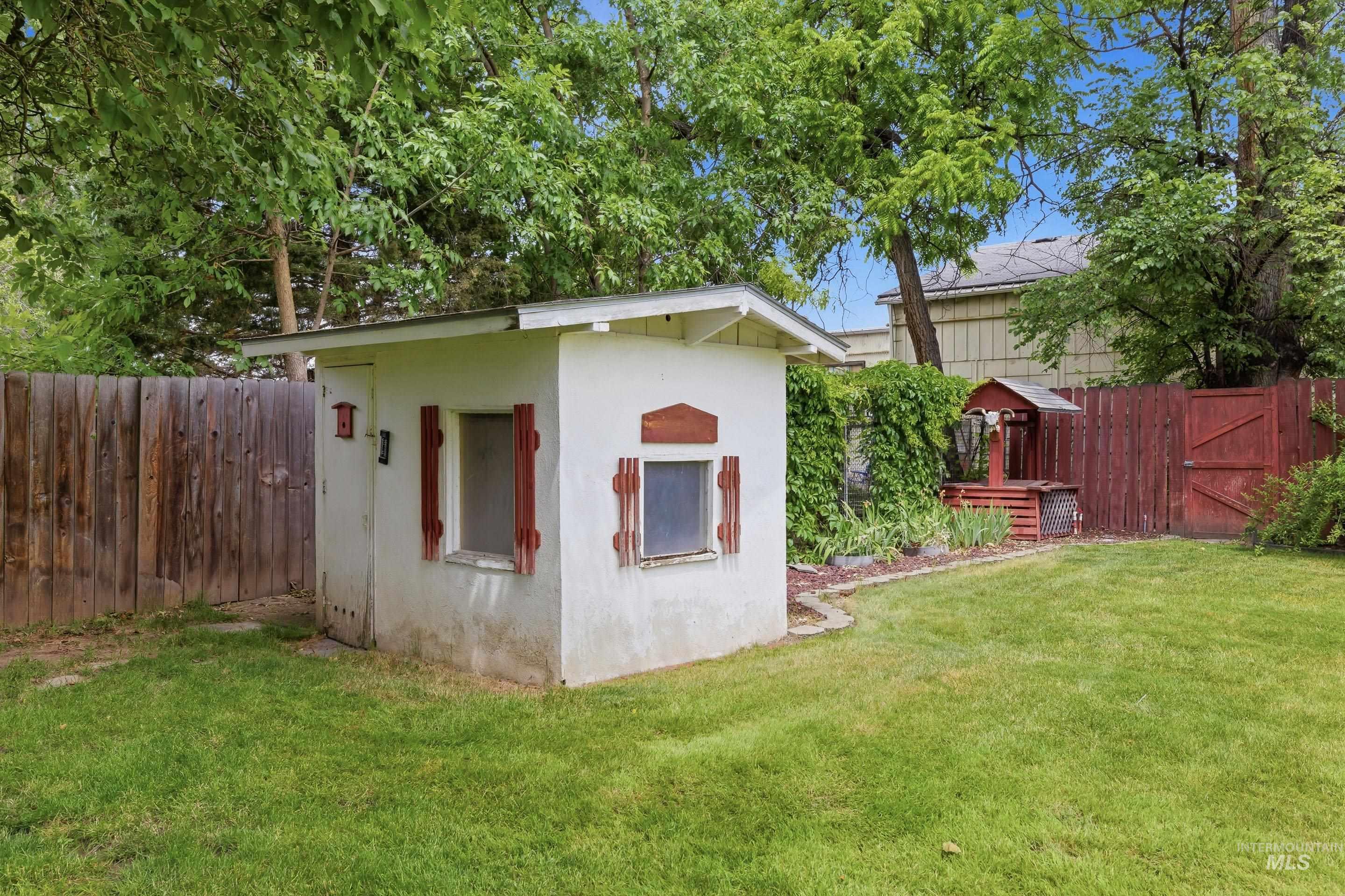 504 West Howe Street Boise, ID 83706 - Photo 43 of 47 Backyard featuring a stucco utility shed with red shutters, wooden fencing, and a manicured lawn