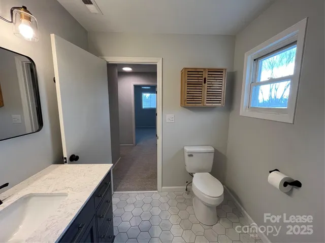a bathroom with a granite countertop sink toilet a large mirror and a window
