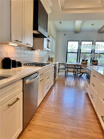 a kitchen with stainless steel appliances granite countertop a sink a stove and white cabinets with wooden floor