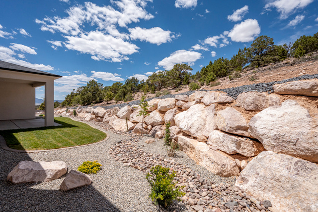 2862 South Mountain Rnch Road Cedar City, UT 84720 - Photo 56 of 64 Manicured lawn area with a curved border of decorative gravel, large natural stone retaining wall, and established trees on the hillside