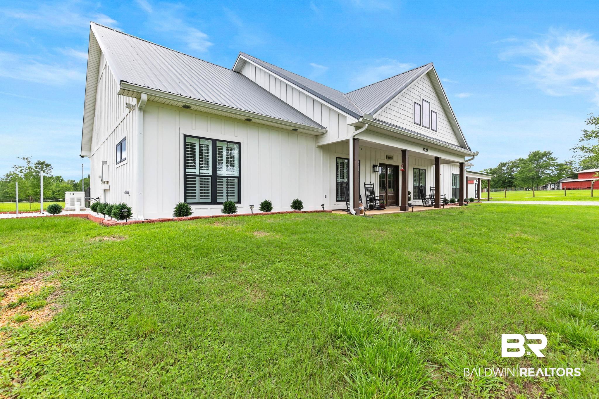 2029 George Lee Road Repton, AL 36475 - Photo 5 of 58 Modern farmhouse exterior featuring white board and batten siding, a metal roof, and a covered front porch with dark wood columns