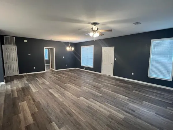 a view of an empty room with wooden floor and a ceiling fan