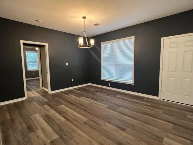 an empty room with wooden floor chandelier and front door