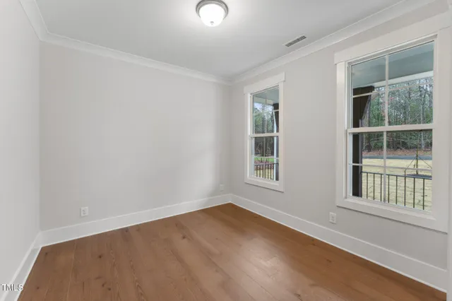 a view of an empty room with wooden floor and windows
