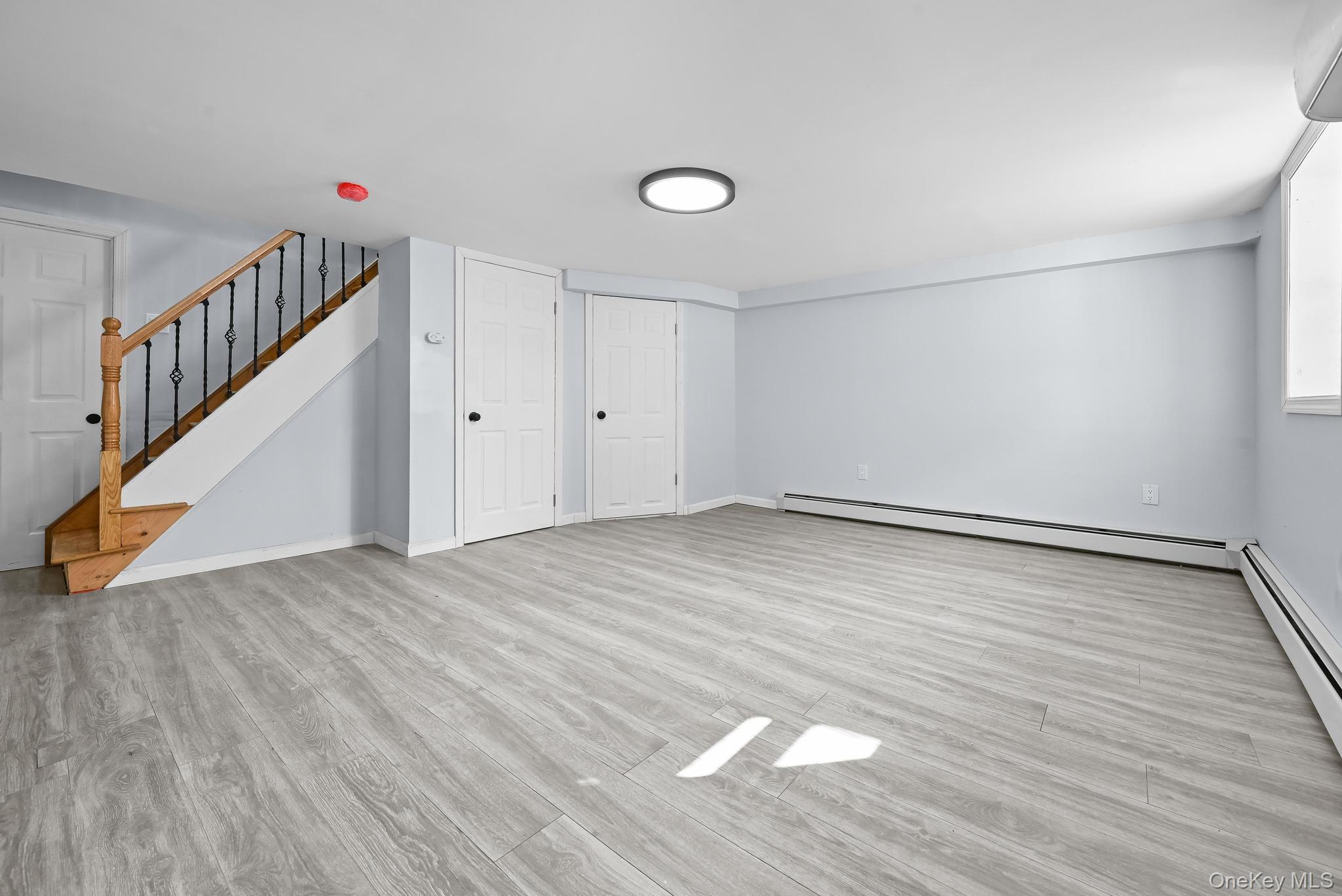 90-04 24th Road Queens, NY 11369 - Photo 11 of 20 Unfurnished living room with light wood-style floors, a baseboard radiator, stairway, and an AC wall unit