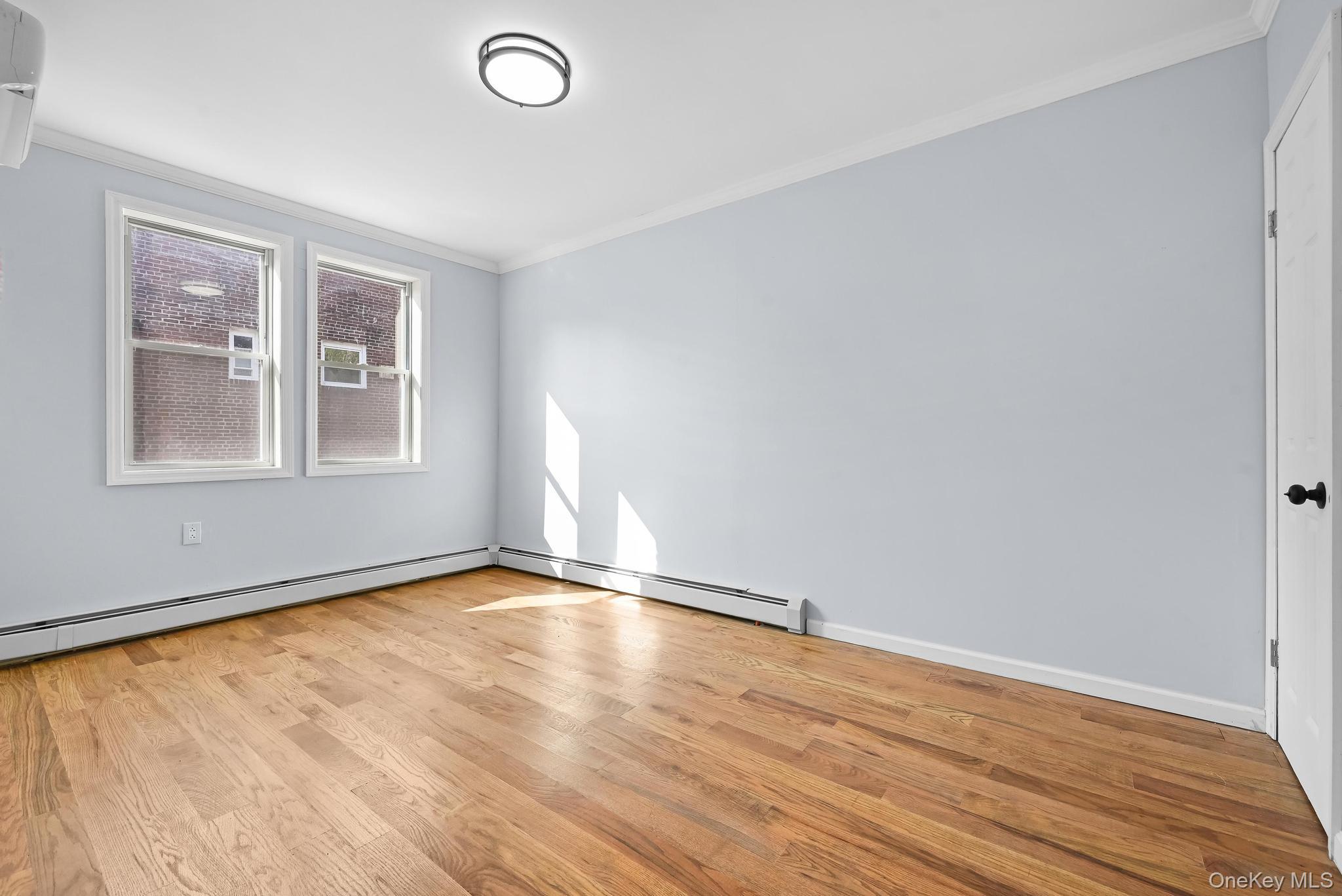 90-04 24th Road Queens, NY 11369 - Photo 13 of 20 Spare room with ornamental molding, light wood-style floors, a baseboard heating unit, and a wall mounted AC