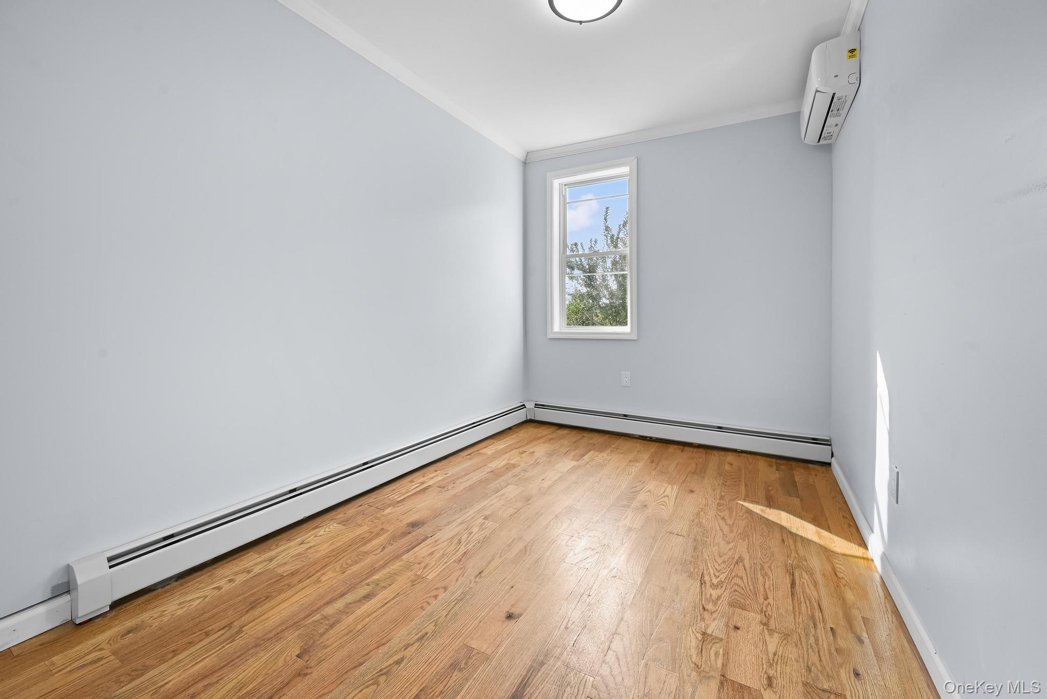 90-04 24th Road Queens, NY 11369 - Photo 14 of 20 Spare room featuring baseboard heating, light wood-type flooring, ornamental molding, and a wall mounted AC