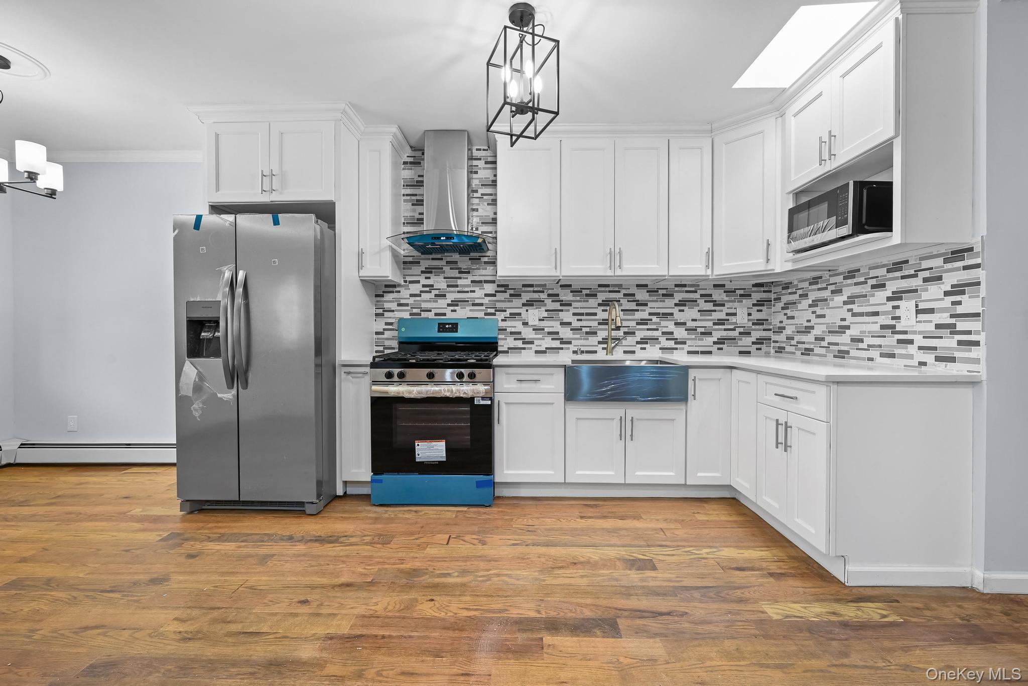 90-04 24th Road Queens, NY 11369 - Photo 7 of 20 Kitchen featuring appliances with stainless steel finishes, white cabinetry, wall chimney range hood, pendant lighting, and crown molding