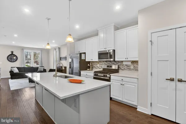 a large white kitchen with kitchen island a stove a sink a refrigerator and white cabinets with wooden floor