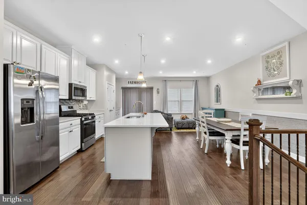 a kitchen with stainless steel appliances kitchen island granite countertop a stove top oven a refrigerator a dining table and chairs with wooden floor