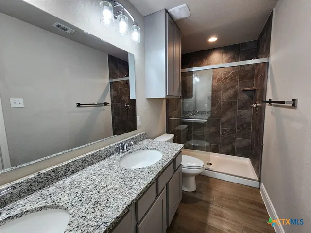 a bathroom with a granite countertop sink a toilet a mirror and shower