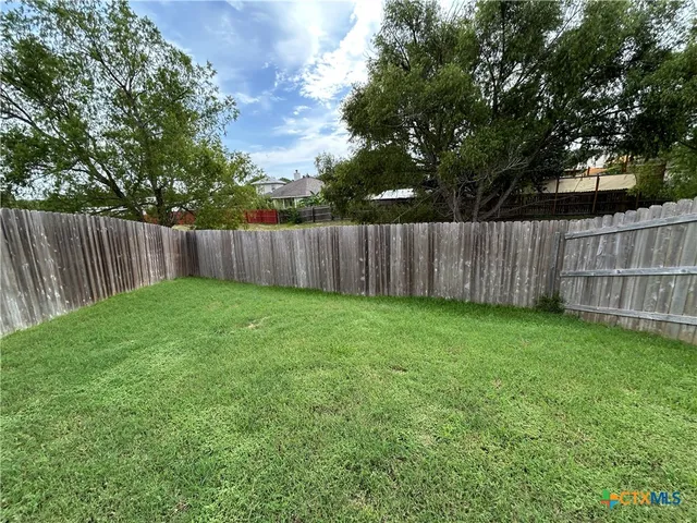 a view of a backyard with large trees and wooden fence