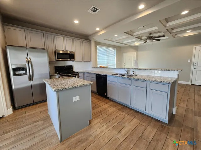 a kitchen with kitchen island granite countertop wooden floors stainless steel appliances a sink and a window