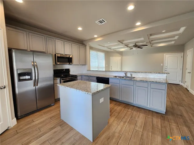 a kitchen with kitchen island granite countertop wooden floors stainless steel appliances and sink