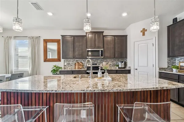 a kitchen with kitchen island granite countertop a table chairs microwave and refrigerator