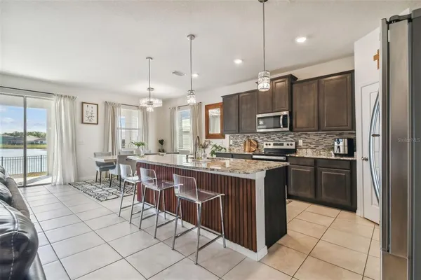 a kitchen with stainless steel appliances kitchen island granite countertop a refrigerator a sink a stove and chairs