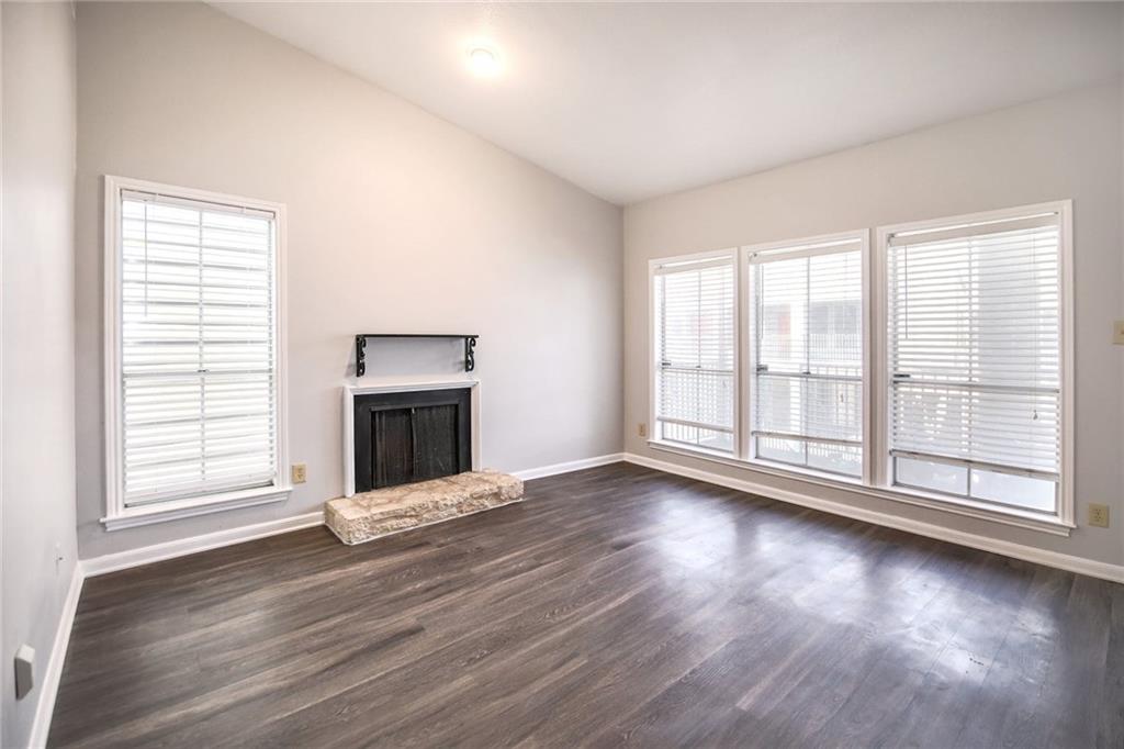 Living area featuring dark wood flooring, a fireplace with a stone hearth, and large windows providing natural light
