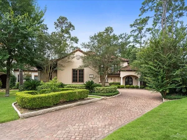 a white house with a big yard plants and large trees