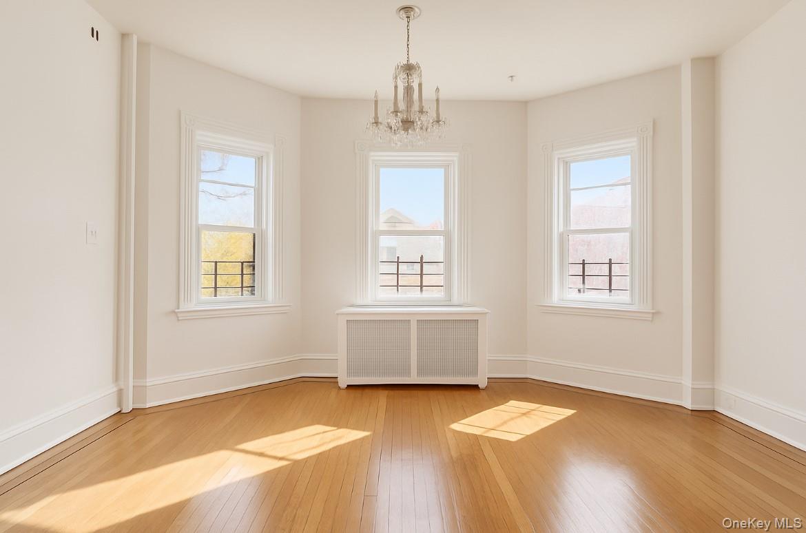194 Summit Avenue, Unit 2 Mount Vernon, NY 10550 - Photo 16 of 19 Empty room featuring radiator, a chandelier, healthy amount of natural light, and light wood-style flooring