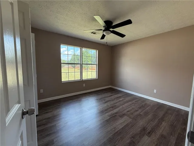 an empty room with wooden floor fan and windows