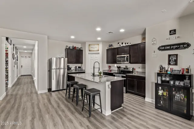 a kitchen with stainless steel appliances kitchen island granite countertop a refrigerator a stove top oven a sink dishwasher and white cabinets with wooden floor