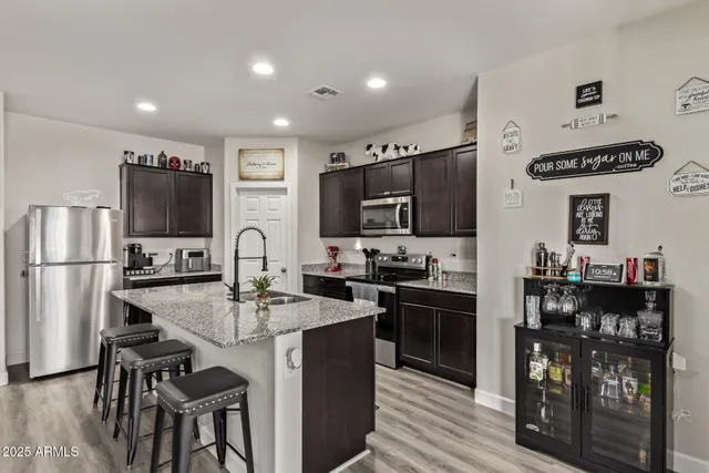 a kitchen with stainless steel appliances granite countertop a stove top oven a sink dishwasher and a refrigerator with wooden floor