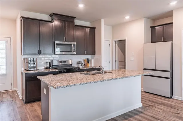 a kitchen with stainless steel appliances granite countertop a refrigerator a stove and a sink with wooden floor