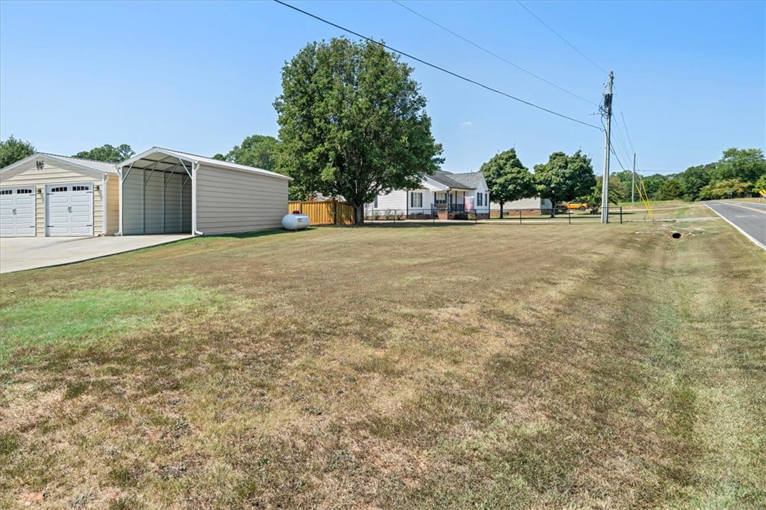623 New Hope Road Anderson, SC 29626 - Photo 47 of 49 A spacious grassy lawn borders the driveway and detached outbuildings under a clear blue sky.