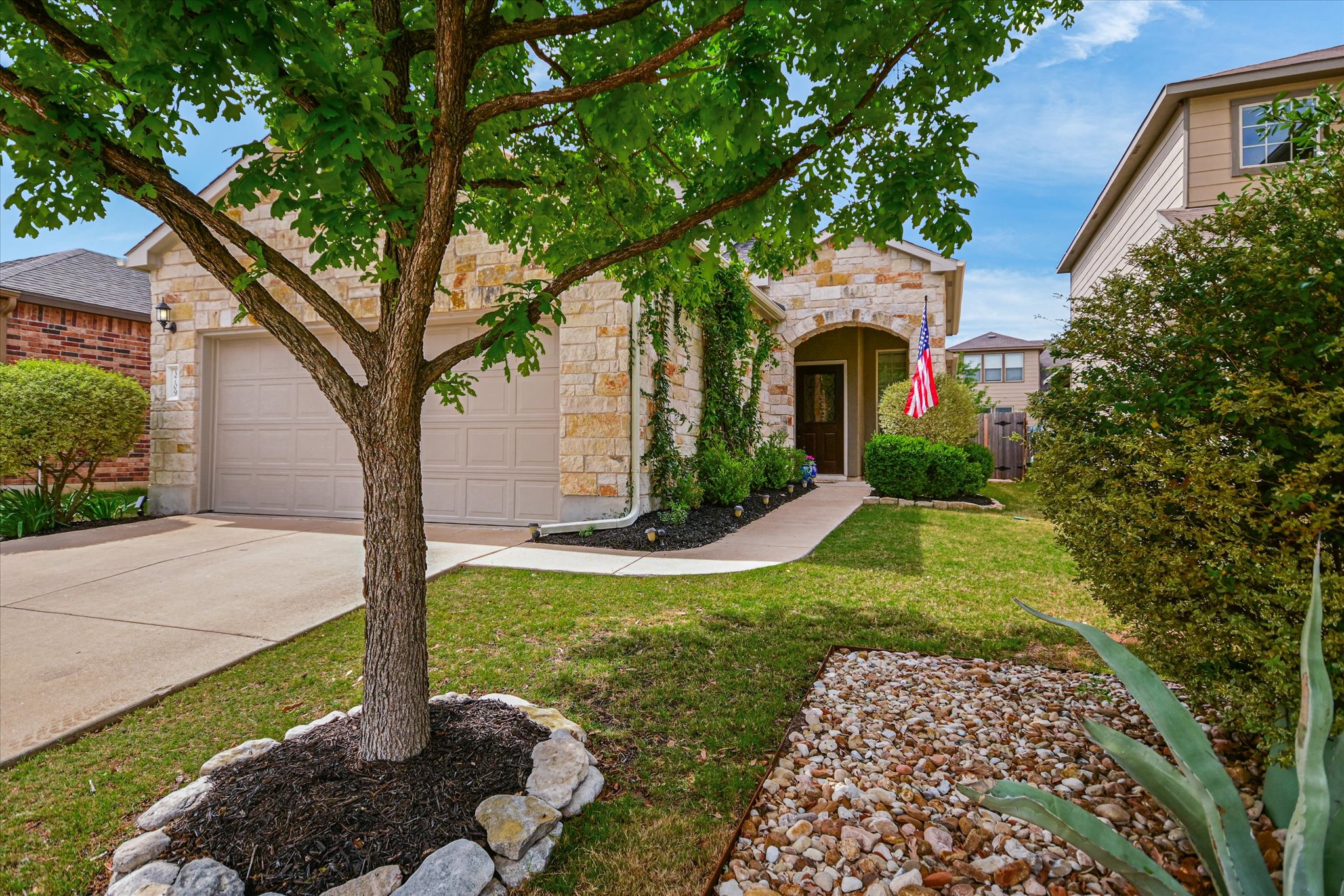 View of front of property featuring stone siding, a front yard, driveway, and a garage