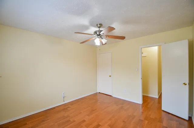 a view of an empty room with chandelier fan and wooden floor