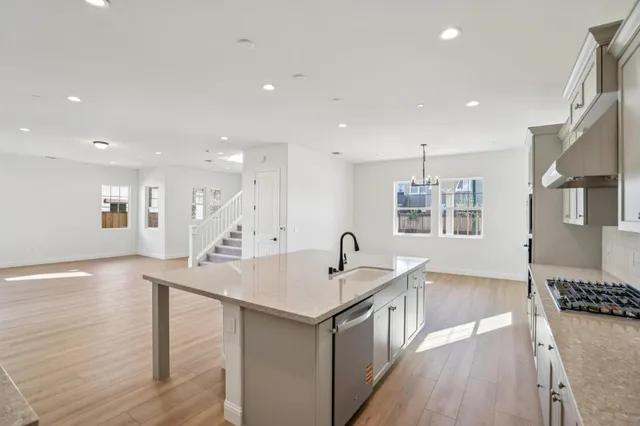 a view of a livingroom with furniture wooden floor kitchen chandelier and windows
