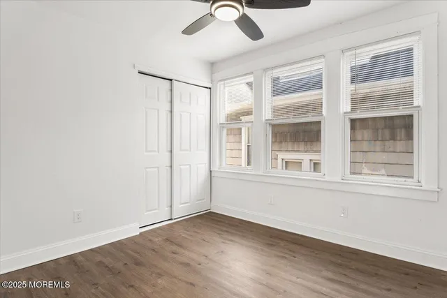 an empty room with wooden floor fan and windows