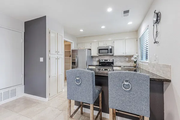 a kitchen with kitchen island granite countertop a refrigerator a stove top oven a sink dishwasher and white cabinets with wooden floor