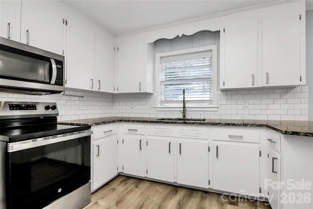 a kitchen with granite countertop white cabinets appliances and a sink