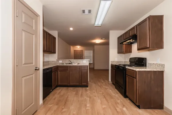a kitchen with stainless steel appliances granite countertop a stove top oven a sink dishwasher and a refrigerator with wooden floor
