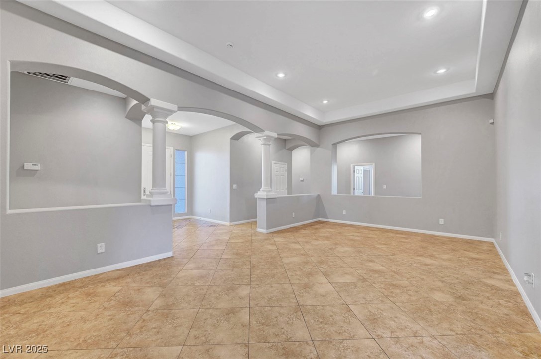 9417 Wisdom Valley Avenue Las Vegas, NV 89149 - Photo 9 of 67 Unfurnished room with arched walkways, a tray ceiling, ornate columns, recessed lighting, and light tile patterned flooring