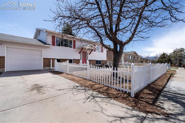 View of front of house with a garage, a fenced front yard, concrete driveway, and brick siding