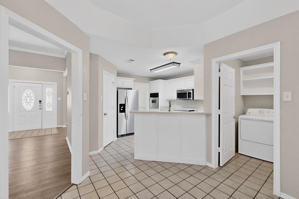 2601 Trail Tree Court Burleson, TX 76028 - Photo 15 of 40 Kitchen with washer / dryer, light countertops, white cabinets, stainless steel appliances, and light tile patterned floors