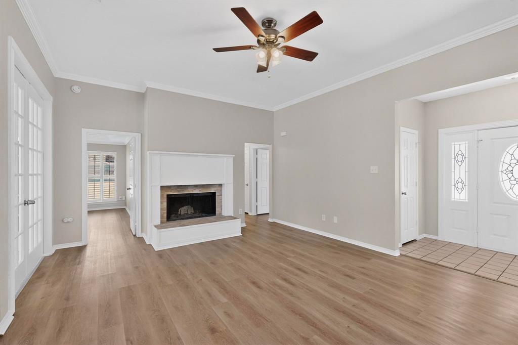 2601 Trail Tree Court Burleson, TX 76028 - Photo 10 of 40 Unfurnished living room with a brick fireplace, a ceiling fan, light wood-type flooring, and crown molding