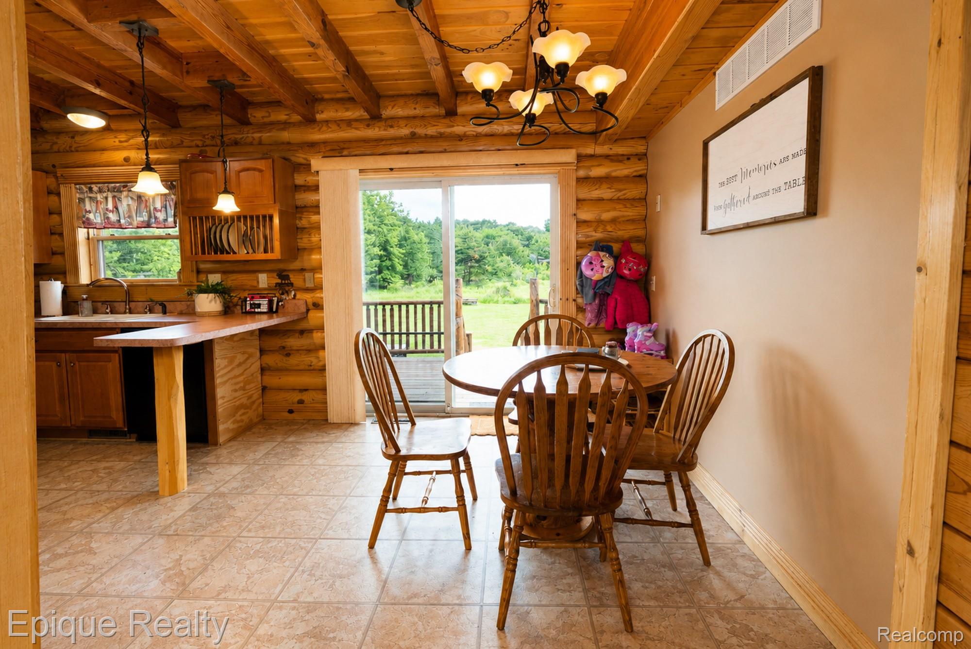 1966 Mayer Road Smiths Creek, MI 48074 - Photo 10 of 38 Log-style interior featuring a kitchen with wood cabinetry and a breakfast bar, an adjacent dining area with a chandelier, and sliding glass doors opening to an outdoor deck