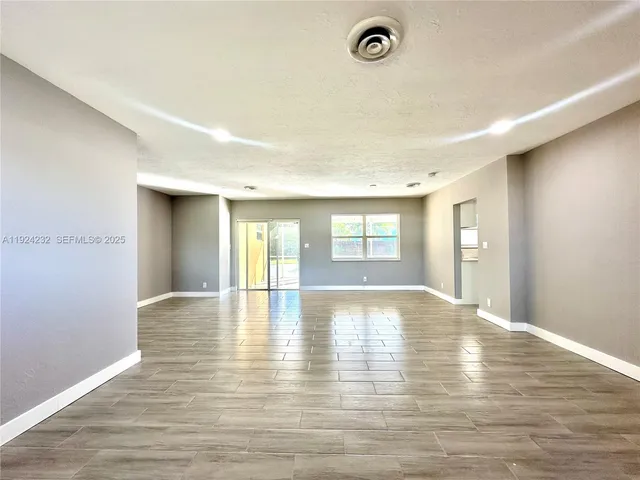 a view of an empty room with window and wooden floor
