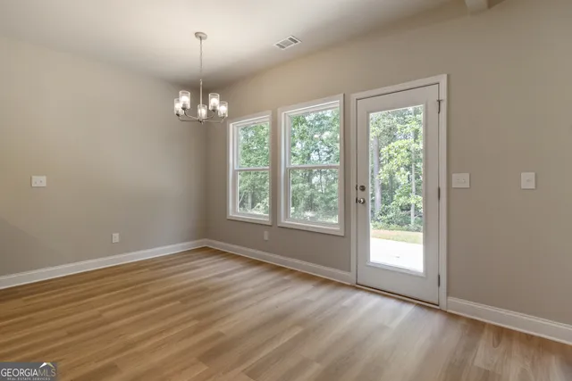 an empty room with wooden floor chandelier and windows