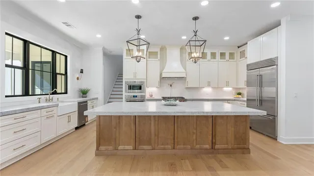 a large white kitchen with granite countertop a stove a sink a refrigerator and white cabinets with wooden floor